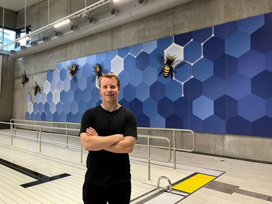 Kunstner Eivind Blaker foran kunstverket "Busy Bees" i Ottestad svømmehall